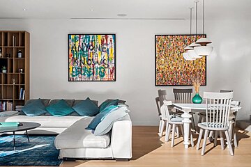 Bright, modern living-dining room with colorful abstract art, a white sectional sofa, and a dining table with white chairs.