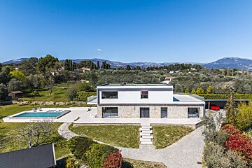 An aerial shot of a modern, two-story luxury villa with a swimming pool, large lawn, and mountain views.