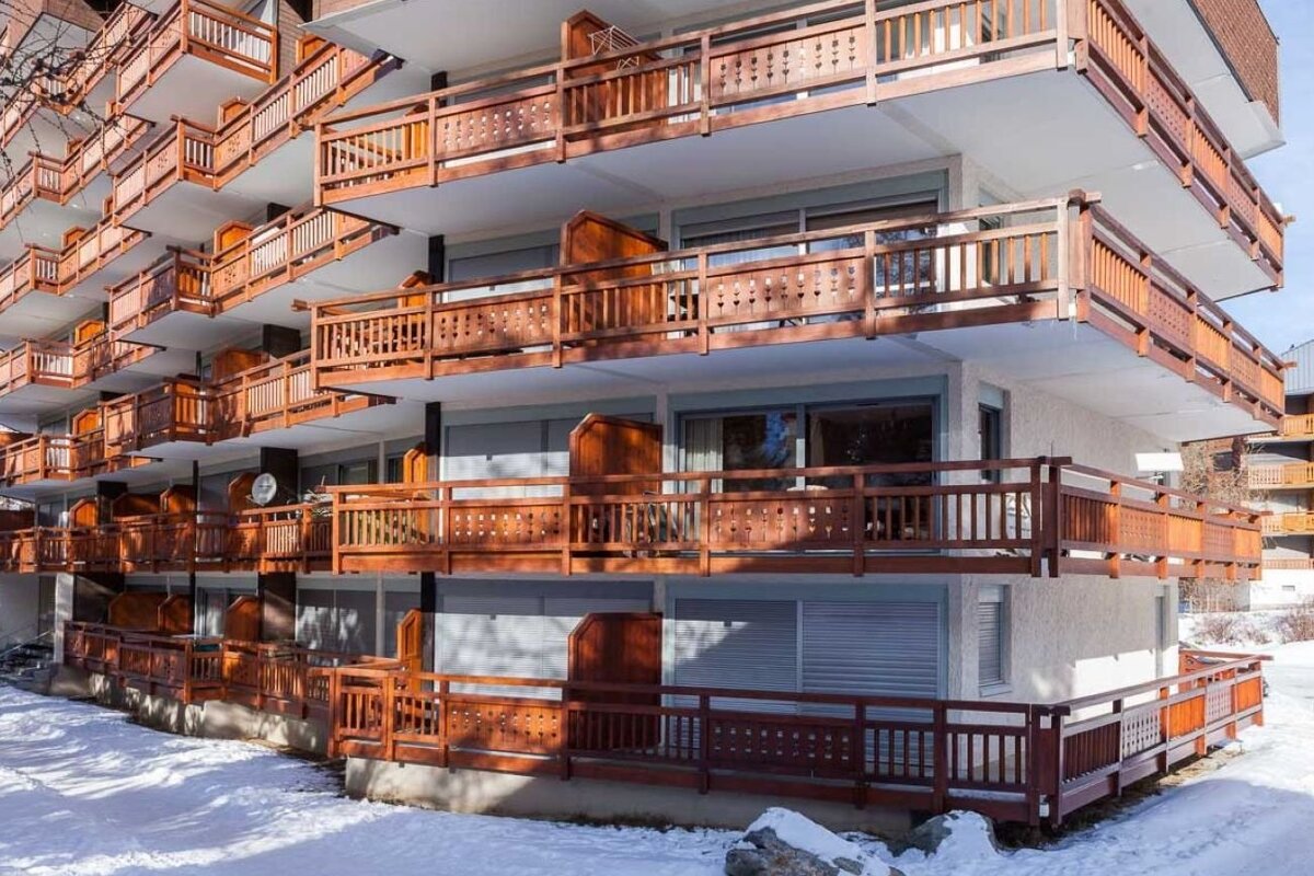 An apartment building with multi-tiered wooden balconies in a snowy winter setting.