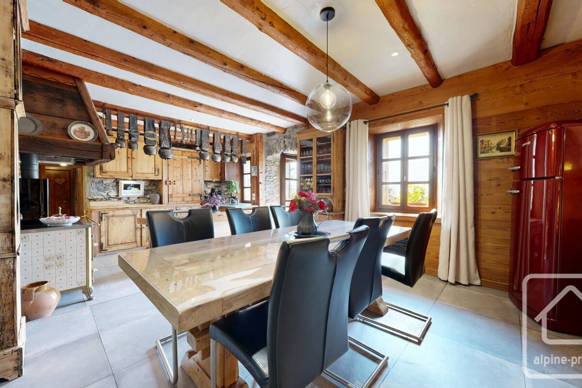 Rustic kitchen/dining room with exposed wooden beams, wooden walls, large dining table, black chairs, and a red retro fridge.