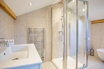 Modern attic bathroom featuring a glass shower, white sink, heated towel rail, and beige tiled walls under a sloped ceiling.