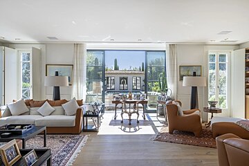 A bright, elegant living room featuring stylish leather furniture and large glass doors looking out onto a beautiful backyard and pool.