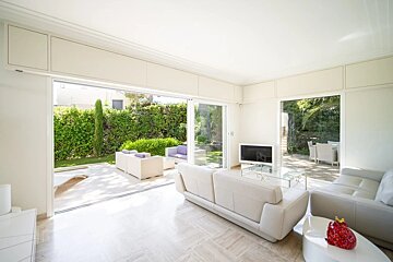 Bright white living room with leather sofas and large sliding glass doors opening to a sunny garden patio.