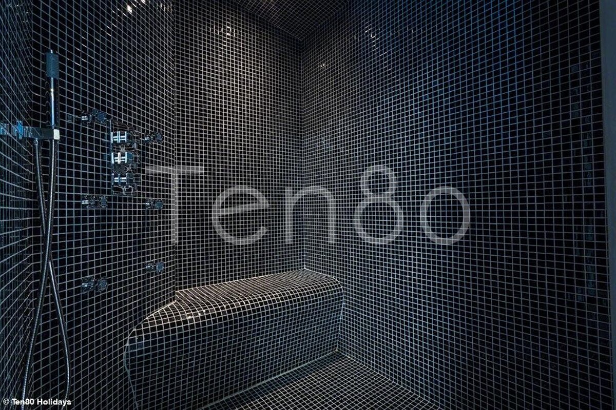Modern steam room tiled in small black mosaics, featuring a built-in bench and chrome fixtures.