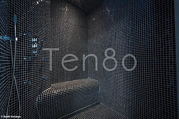Modern steam room tiled in small black mosaics, featuring a built-in bench and chrome fixtures.