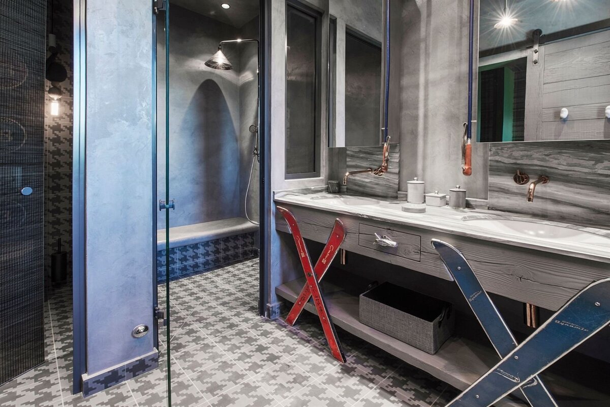 Chic gray bathroom with houndstooth tiles, double sink, copper fixtures, and decorative skis, blending modern and ski lodge aesthetics.