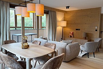 A cozy modern interior featuring a wooden dining table under warm pendant lights and a living room with elegant wood paneling.