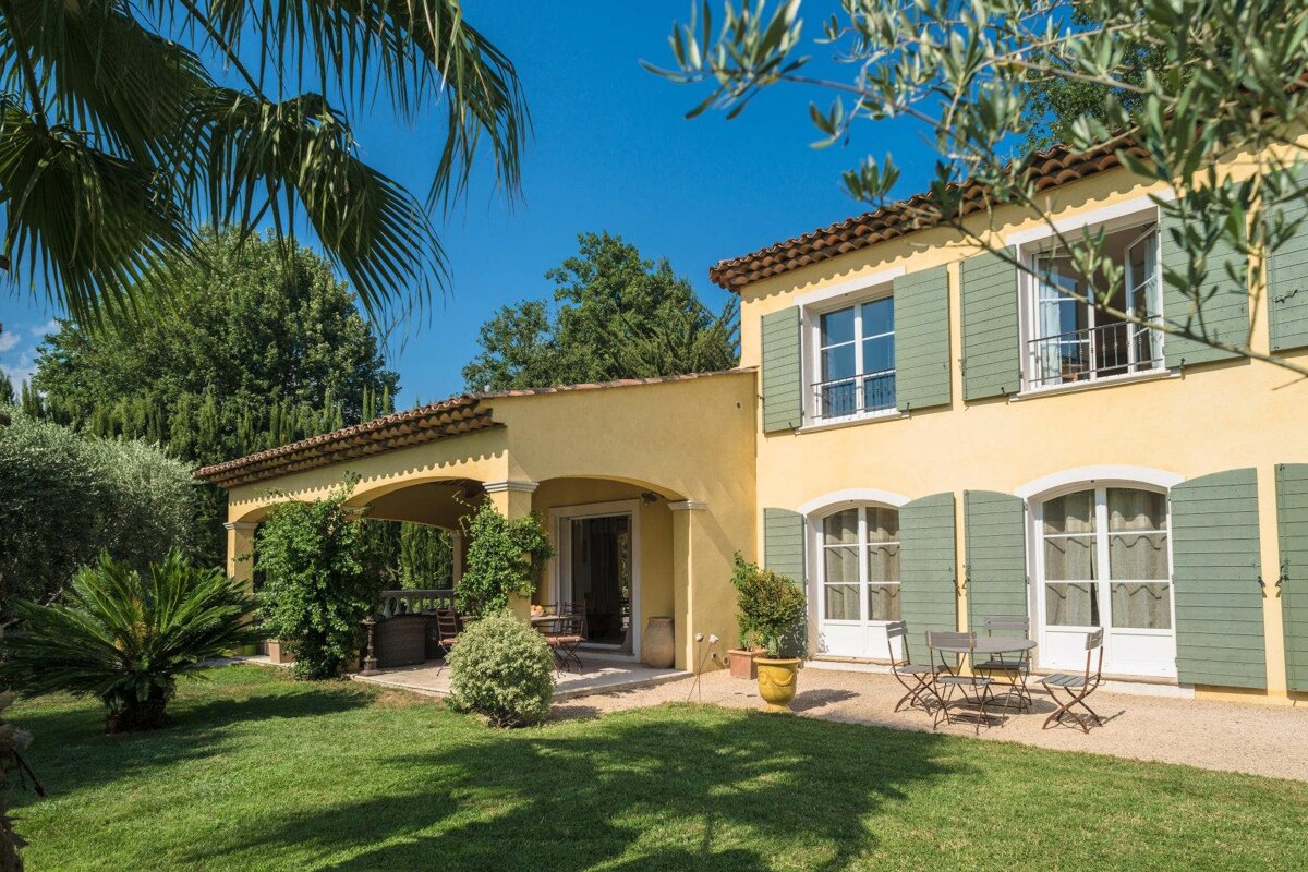 A yellow house with green shutters sits on a lush green lawn