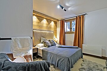 Cozy modern bedroom featuring a wood-paneled accent wall, grey bed, warm lighting, and orange curtains.