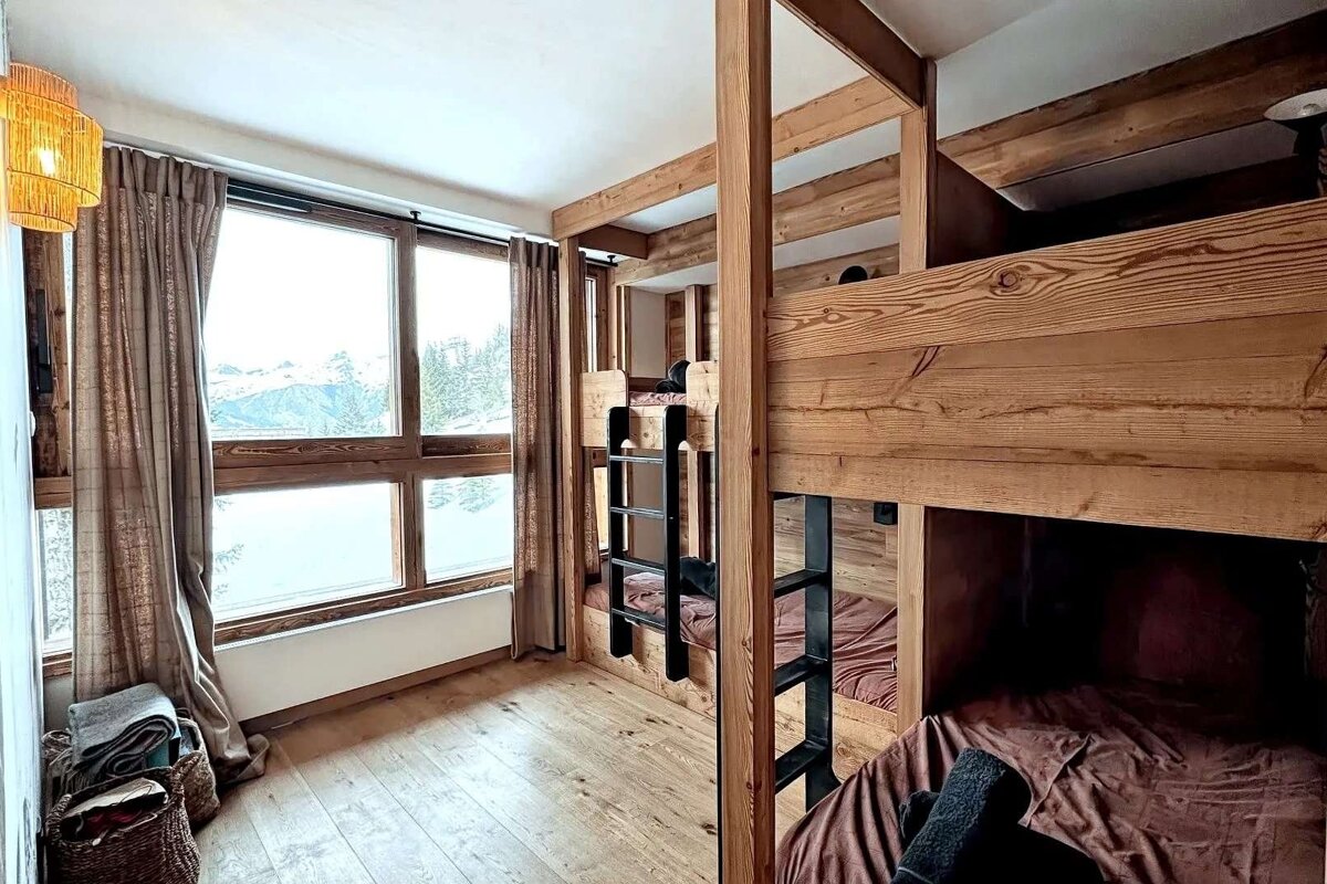 Rustic room with sturdy wooden bunk beds, hardwood floors, and a large window revealing a snowy mountain landscape.