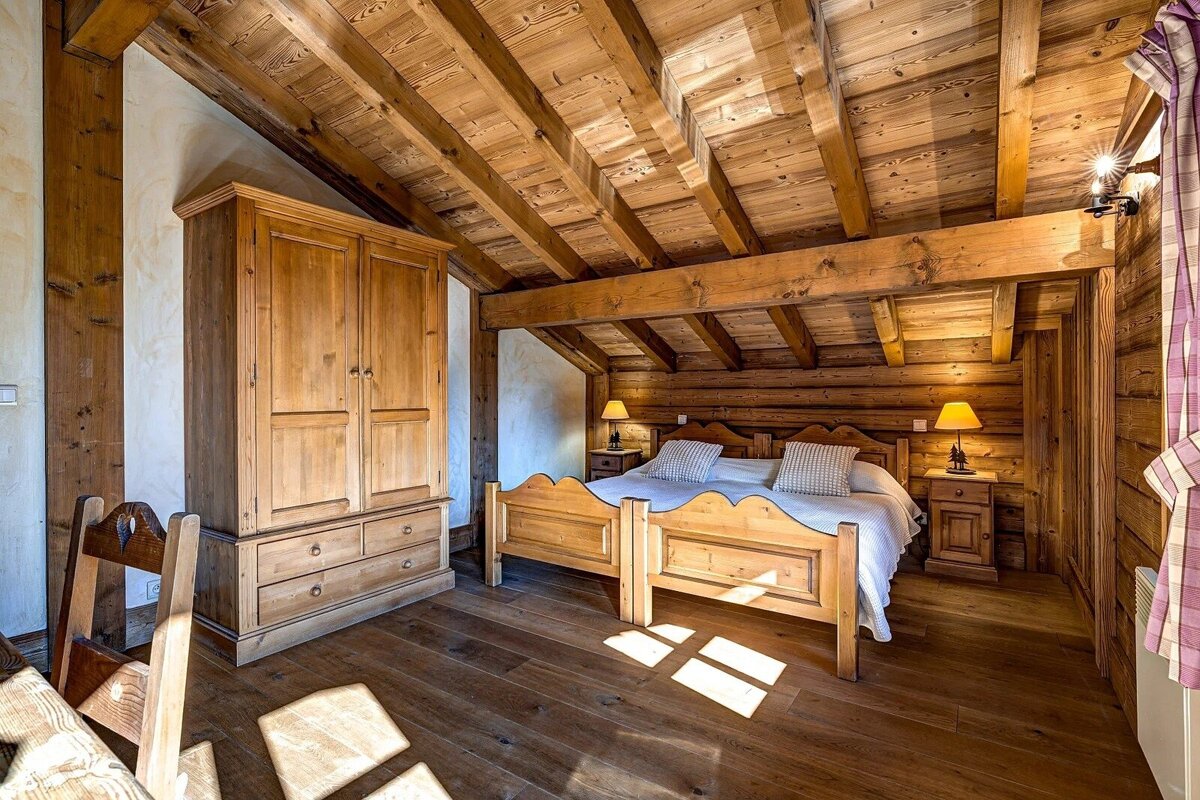 A rustic, all-wood bedroom featuring a large wooden bed, wardrobe, and exposed beams on the ceiling, creating a warm, cozy atmosphere.