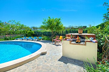 A sunny outdoor patio features a blue swimming pool, lounge chairs, and an active barbecue grill. Lush greenery surrounds the stone ground under a clear blue sky.