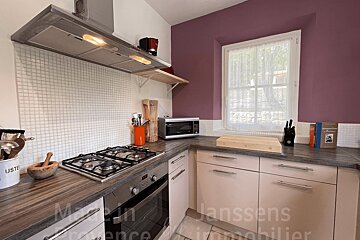 A cozy kitchen with a gas hob, oven, microwave, tiled backsplash, and plum walls, featuring a window with a sheer curtain.