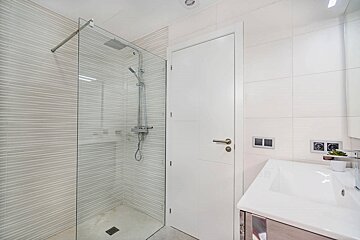 Modern white bathroom with a sleek glass shower enclosure, a white door, and a sink with chrome fixtures.