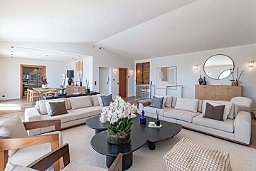 Bright, open-plan living room with two large cream sofas, a modern dark coffee table adorned with white orchids, and a dining area beyond.