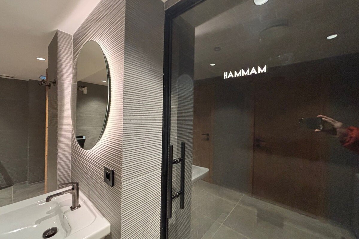 A modern bathroom with a sink, backlit oval mirror, and a glass door to a 