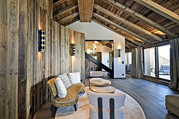 Modern rustic chalet interior with wood walls/ceiling, stylish furniture, large windows, and a sleek staircase.
