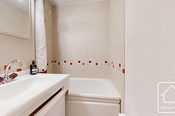 A bathroom with a sink and a bathtub with a bottle of shampoo on the counter