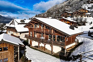 Snow-covered wooden chalets on a sunny mountain slope under a bright blue sky. An idyllic alpine winter village.
