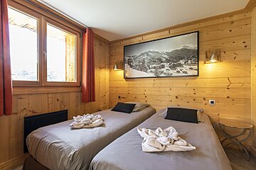 A wooden bedroom with two single beds, a mountain photo on the wall, and a large window.