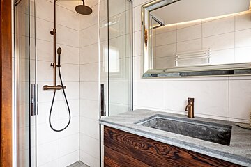 Modern bathroom featuring a glass shower with bronze fixtures, a stone sink with a wooden vanity, and a large framed mirror.