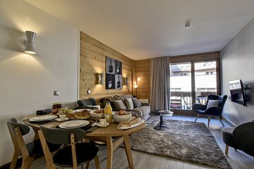 Cozy modern apartment featuring a set dining table, a living area with a grey sofa, rug, armchair, and balcony access.