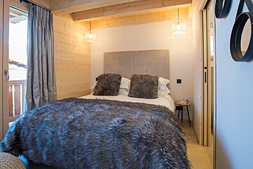 Cozy cabin bedroom featuring a bed adorned with a fluffy grey faux fur blanket, rustic wood walls, and hanging pendant lights.