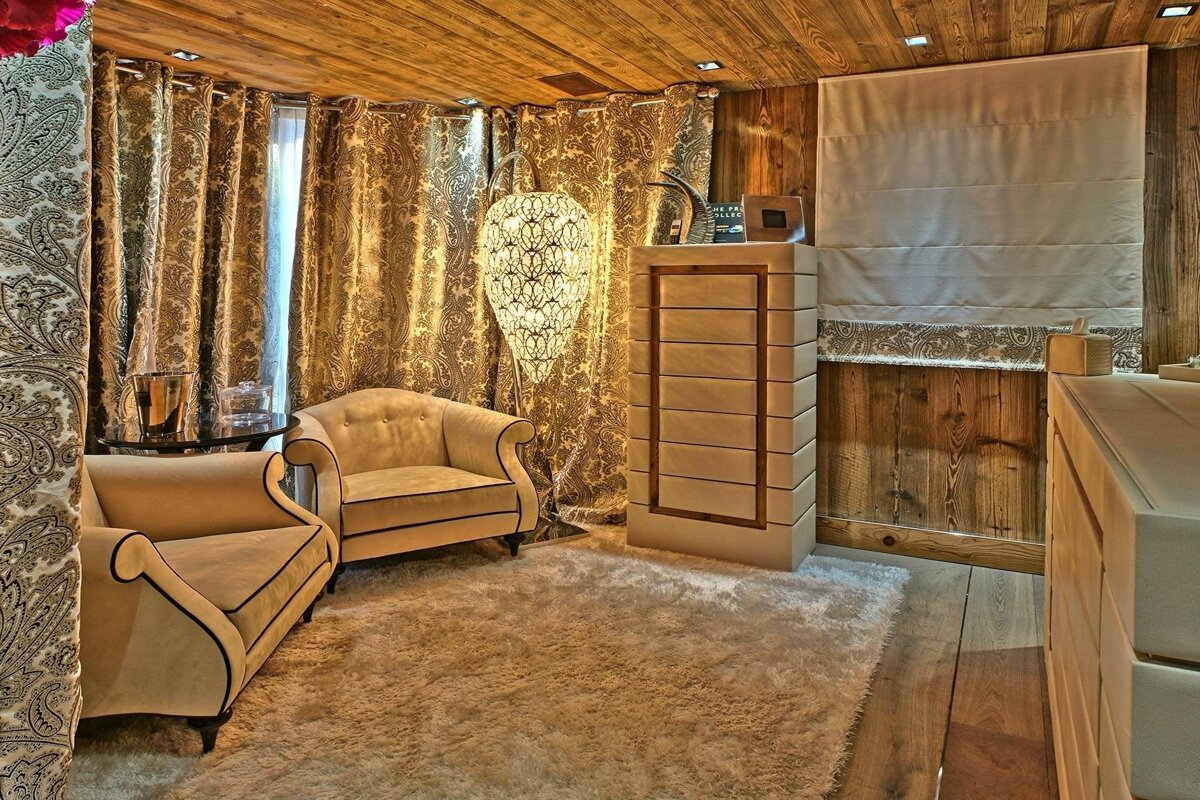 A luxurious room with two beige armchairs, a shaggy rug, paisley curtains, wood paneling, and a decorative floor lamp, creating a cozy ambiance.