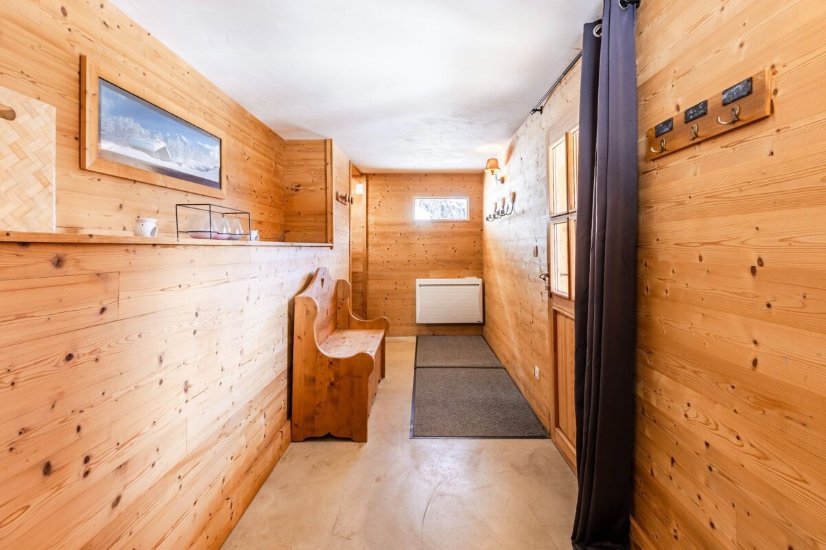 Rustic chalet entryway with light wood-paneled walls, a wooden bench, concrete floor, and a dark curtain.