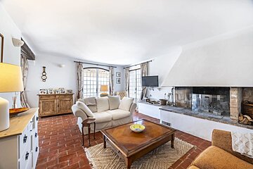 Bright living room with terracotta floor, white walls, a large fireplace, white sofa, wooden coffee table, and arched windows.