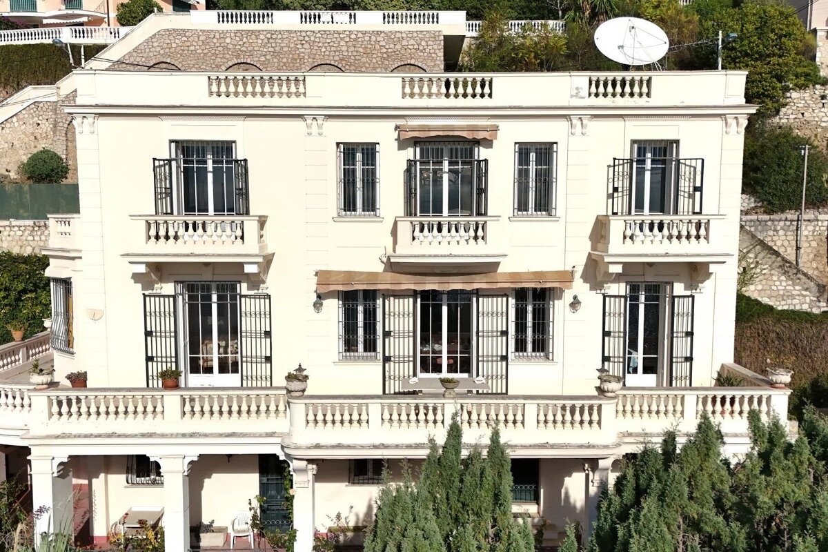 An elegant cream-colored Mediterranean villa featuring multiple balconies with balustrades and black iron window grilles.