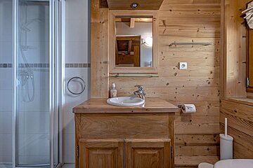 A cozy, wood-paneled bathroom featuring a shower, a sink with a mirror above a wooden vanity, and a toilet in the corner.