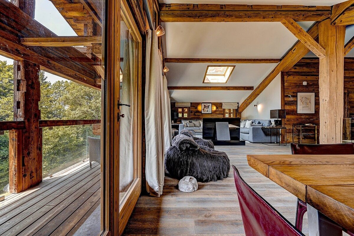 Cozy, rustic modern cabin interior with exposed wood beams, a living area, and a balcony overlooking a lush forest.