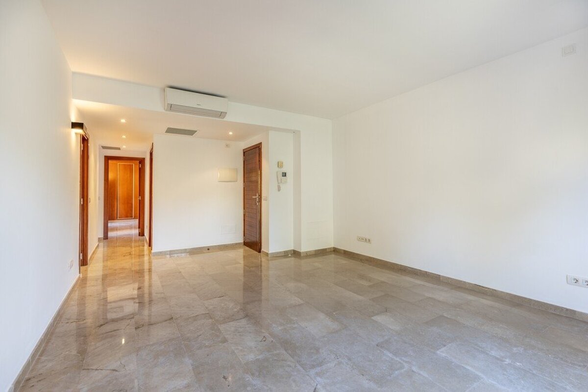 An empty apartment interior featuring shiny marble-tiled floors, white walls, and a hallway leading to wooden doors.