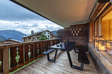 A balcony with a table and benches and a view of the mountains