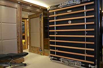 An elegant home gym showcasing a black wall-mounted Technogym system with wooden rungs, an exercise bench, and sophisticated wooden interior design.