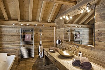 Chalet-style wooden bathroom with a brass vessel sink, large mirror, towel warmer, and cute polar bear decorations.
