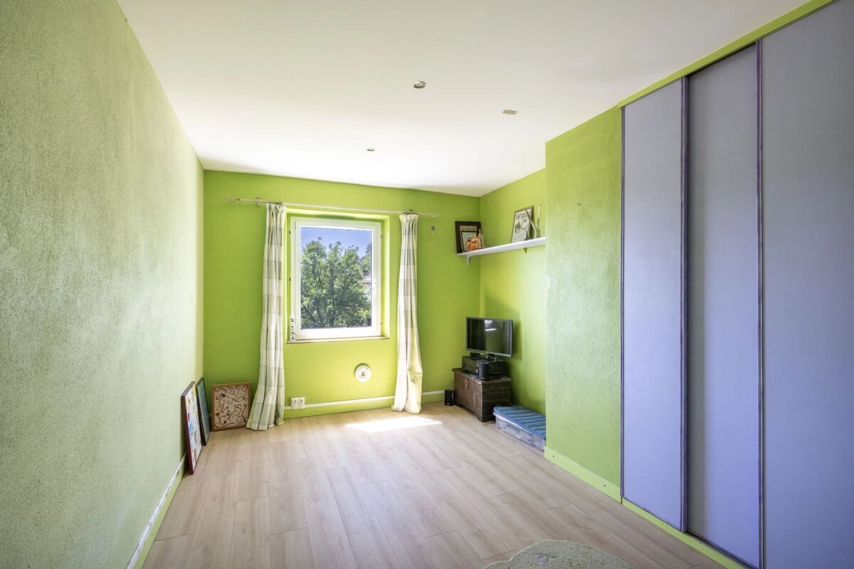 Bright room with lime green walls, a window overlooking trees, wood floor, and light blue sliding closets. A small TV and shelf are visible.
