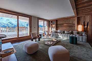 Cozy modern chalet living room with rustic wood walls, elegant furniture, and glass doors overlooking snowy mountain peaks.