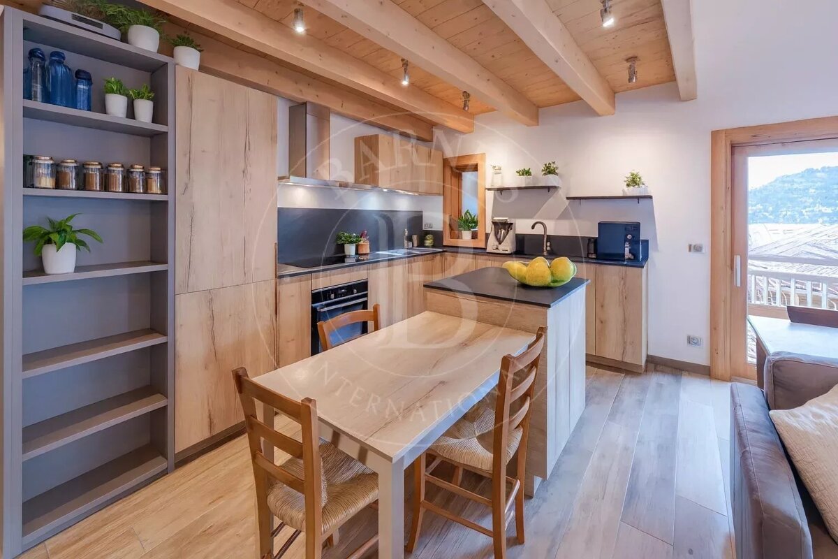Modern rustic kitchen featuring light wood cabinets, exposed wooden ceiling beams, a kitchen island, and a dining table with chairs.