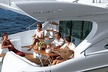 A group of people sitting on a white yacht reading a newspaper