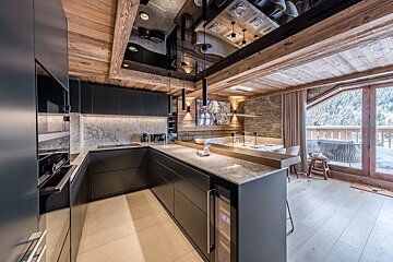 Modern dark kitchen with rustic wood/stone accents, mirrored ceiling, dining area, and snowy balcony view.