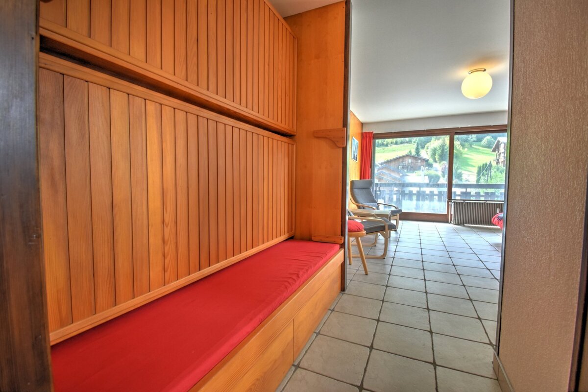 A room featuring a wooden built-in bench with a red cushion, a tiled floor, and a glass door looking out onto a scenic mountain view.