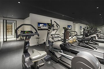 A stylish home gym features modern exercise equipment, TVs displaying 