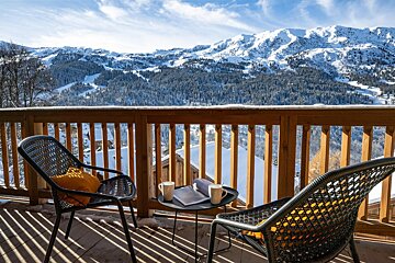 Two chairs and a table on a balcony with mountains in the background