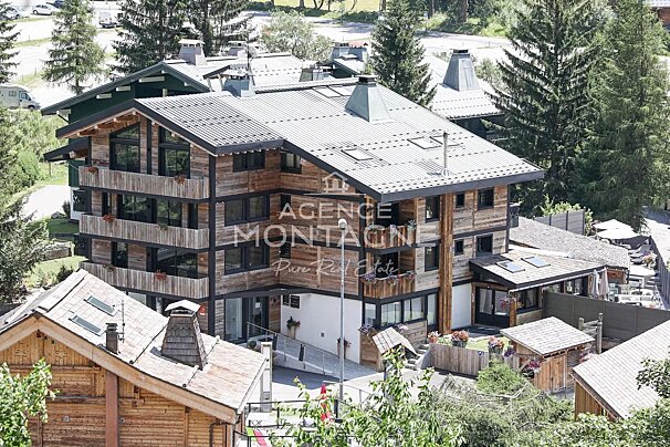An aerial view of a multi-story rustic wooden chalet-style building with balconies, surrounded by lush green trees.