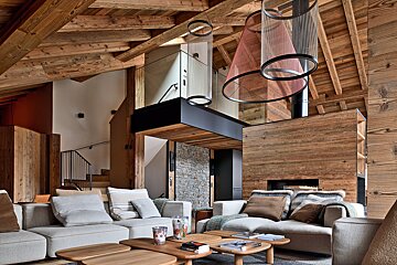 Cozy, modern chalet living room featuring vaulted wooden ceilings, comfortable sofas, and unique mesh pendant lights.