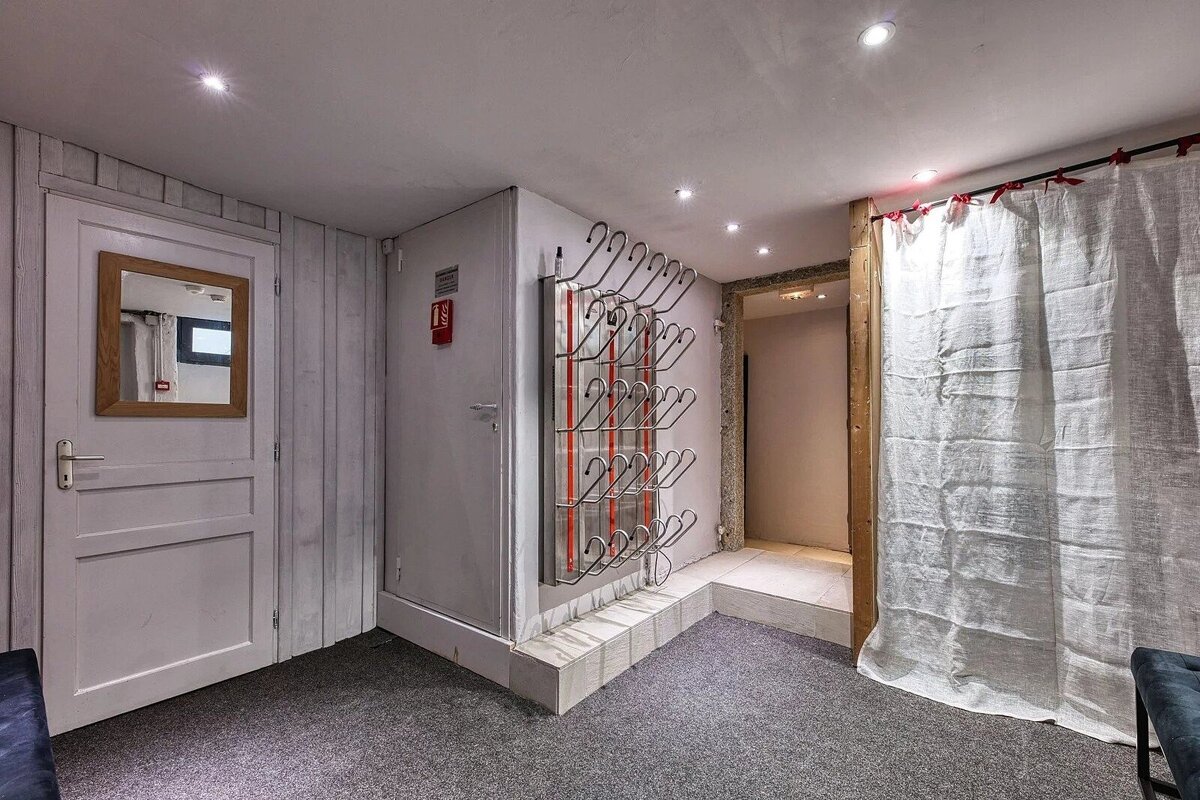 A functional room with gray carpet, white walls, a mirror, and a large boot drying rack, suggesting a ski boot room or changing area.