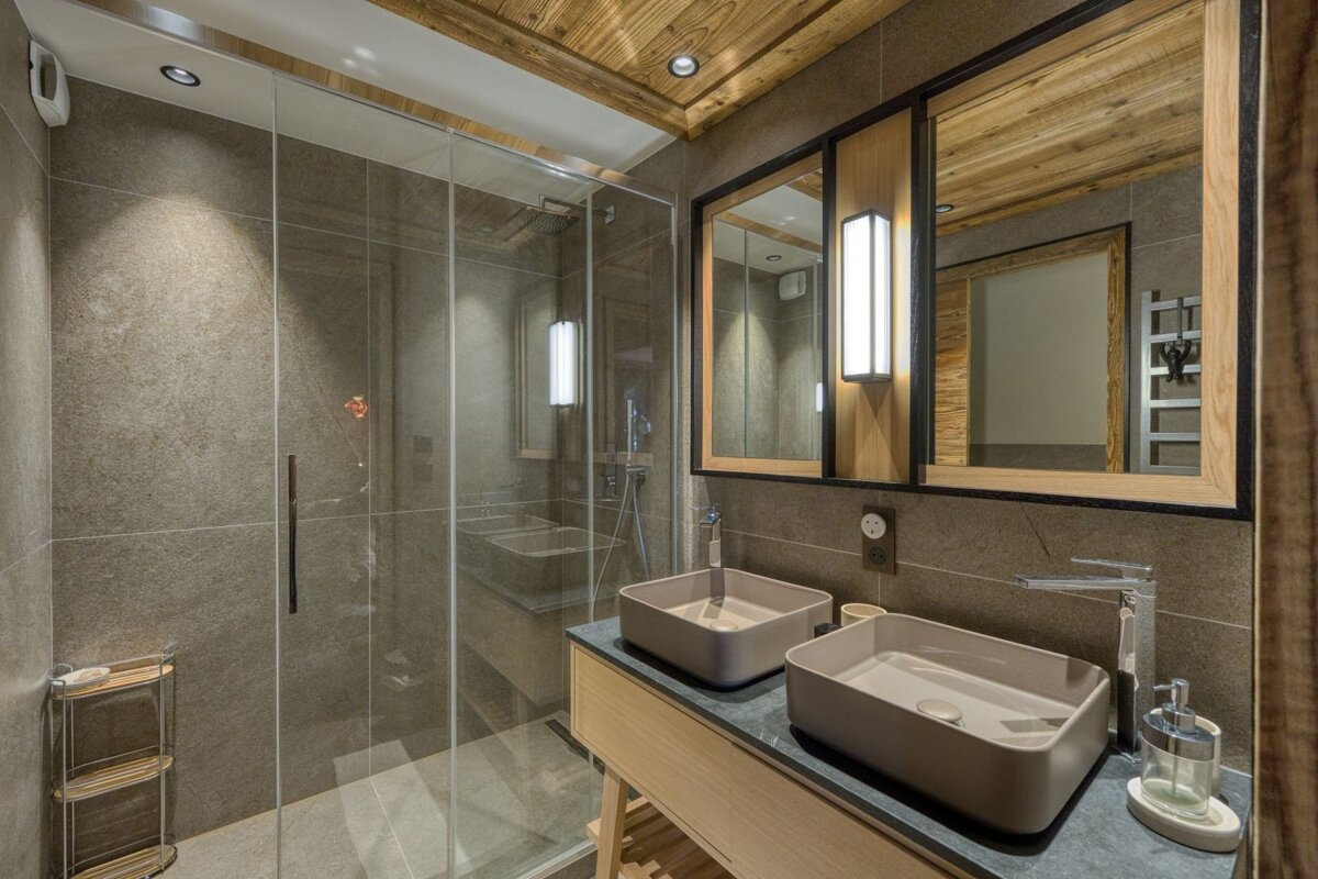 Modern bathroom with glass shower, double vanity, wooden ceiling & accents, and gray tiles.