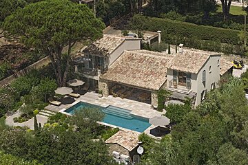 Aerial view of a large Mediterranean-style villa with terra cotta roofs, a blue swimming pool, sun loungers, and lush green gardens.